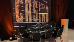 POKERTAFEL MET STOELEN MET DAARACHTER EEN GROOT CASINO DECORATIE DOEK