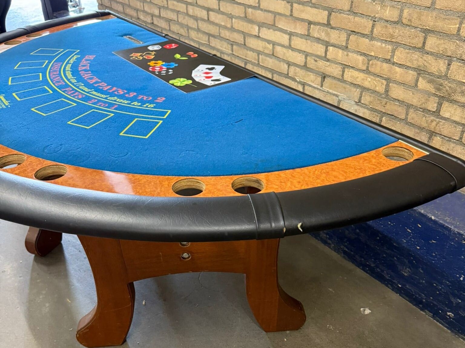 Zijaanzicht van tweedehands blackjacktafel met zwarte skyleren rand en houten details.